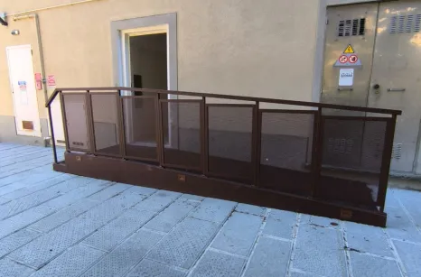 Rampa disabili in acciaio verniciato simil corten con pavimento in lamiera stirata antiscivolo e balaustra con pannelli in lamiera forata